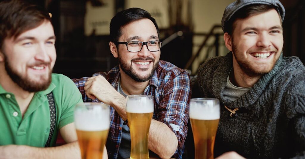 Group of young friends happily enjoying beers together at an indoor pub setting.